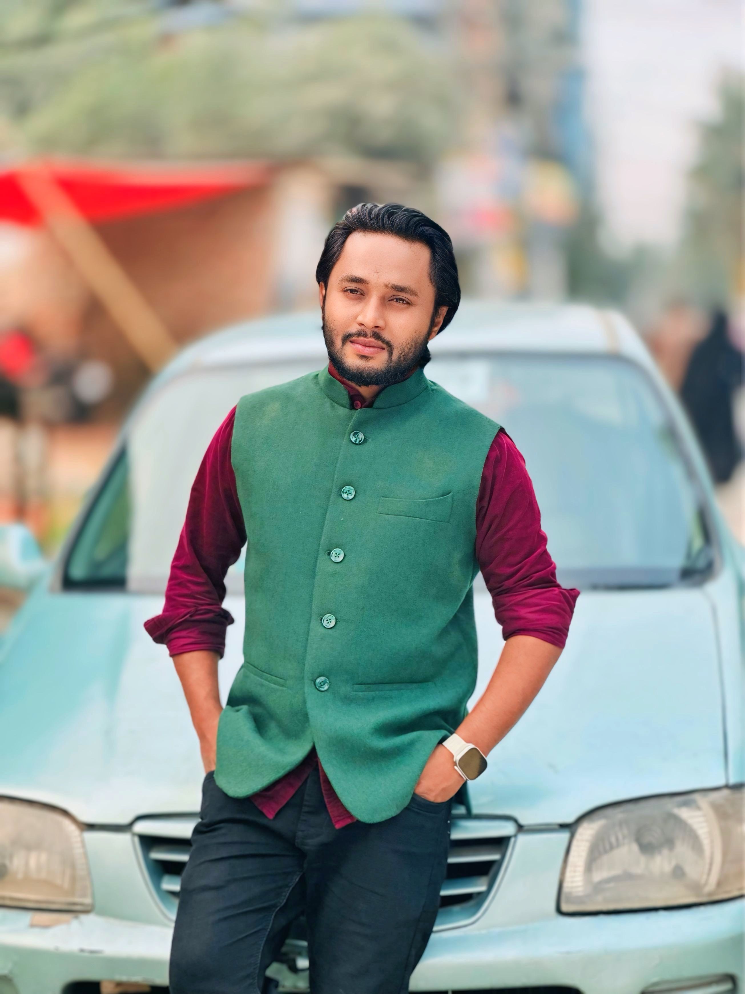 Confident man in green vest stands casually in front of a car, smiling outdoors.
