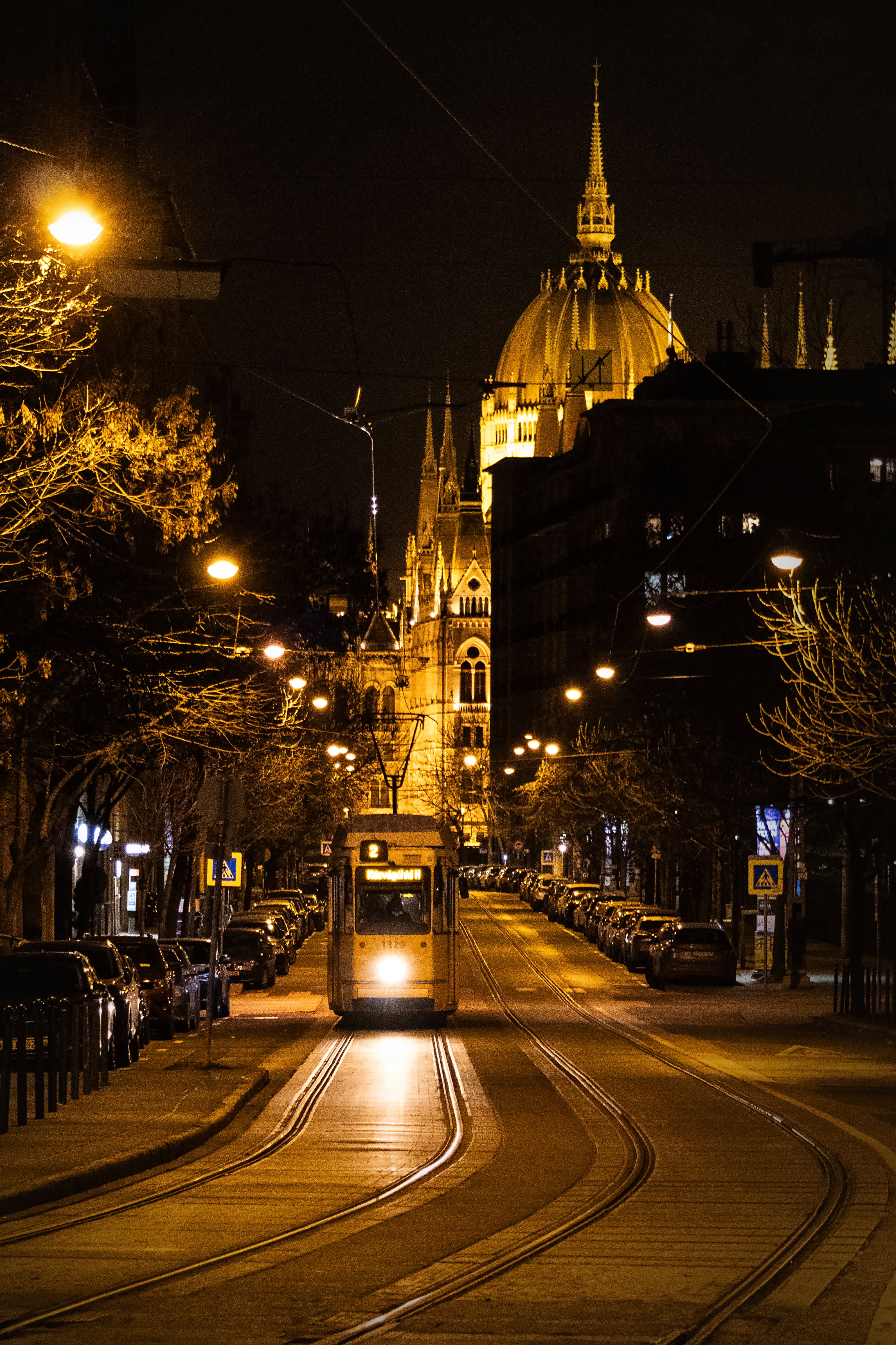 Night view of a tram with Budapest Parliament in the background, beautifully lit.