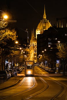 Night view of a tram with Budapest Parliament in the background, beautifully lit.