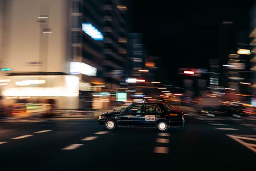 Blurred motion capture of a taxi speeding through a city's bustling night streets.