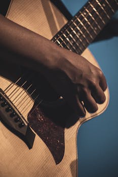 Artistic close-up of a hand strumming an acoustic guitar in soft lighting, creating a moody ambiance.