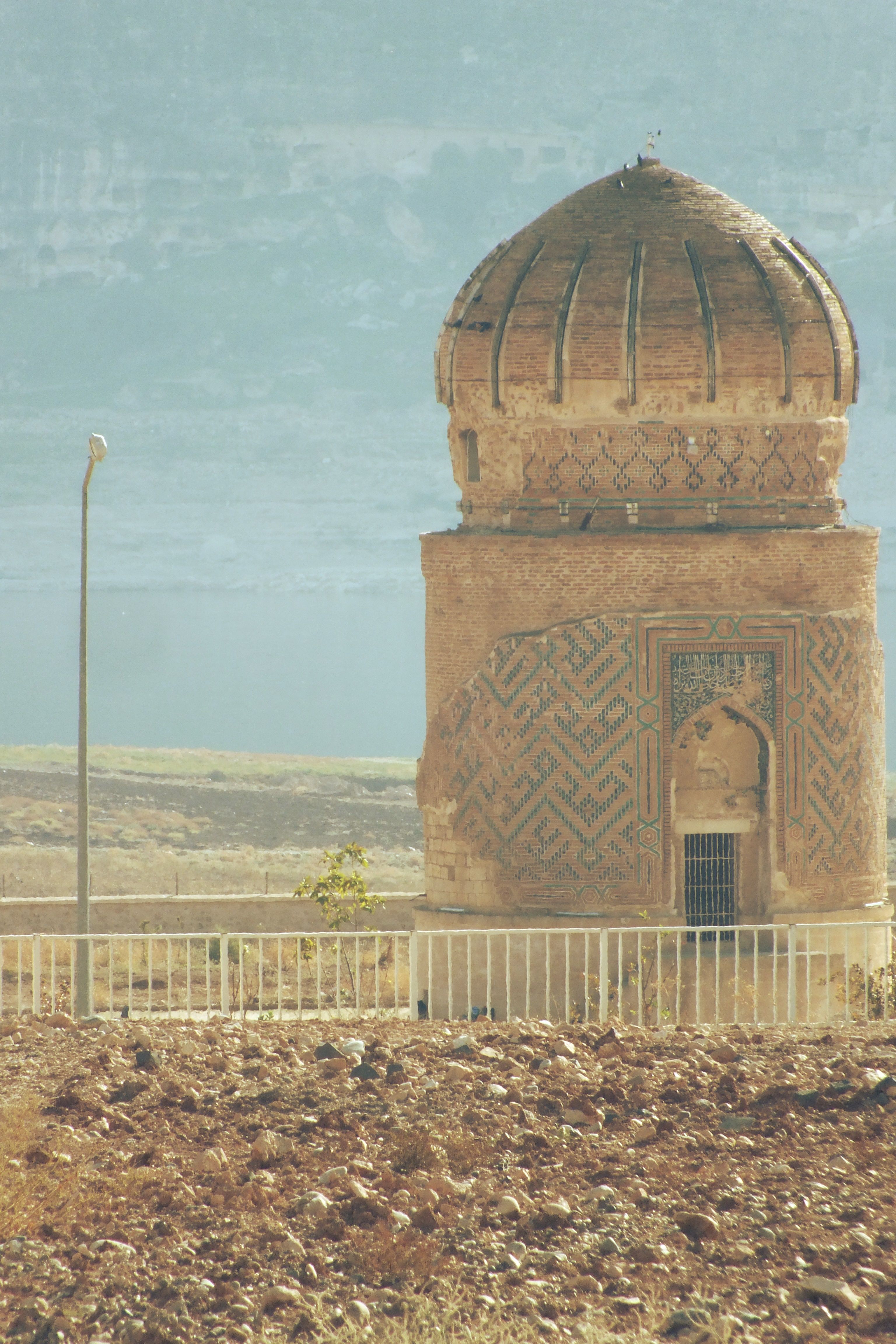Ancient architectural tower in the arid landscape of Mardin, Türkiye, under a bright sky.