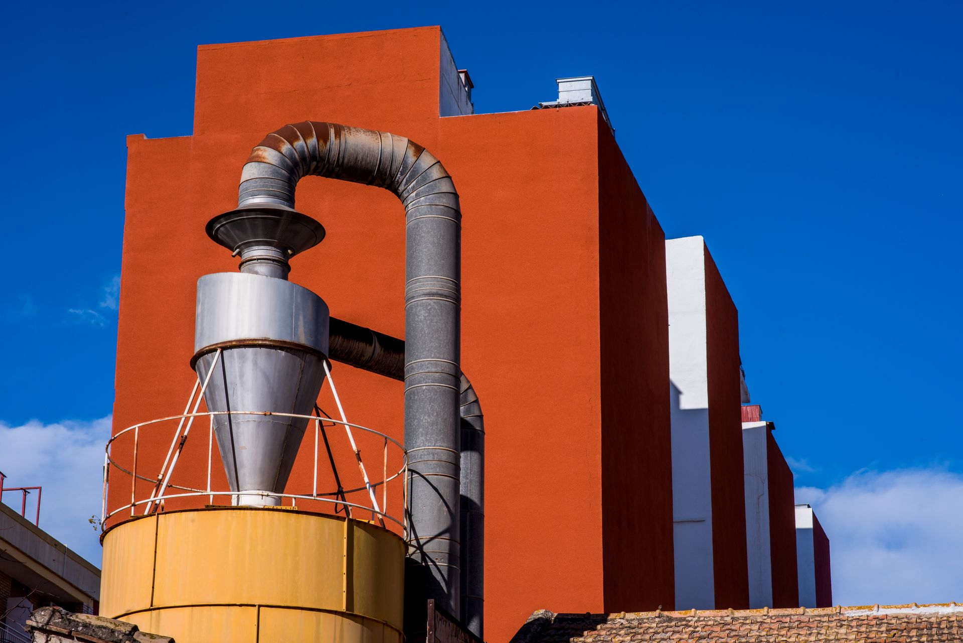 A striking industrial facility with vibrant red walls and metallic machinery against a clear blue sky.