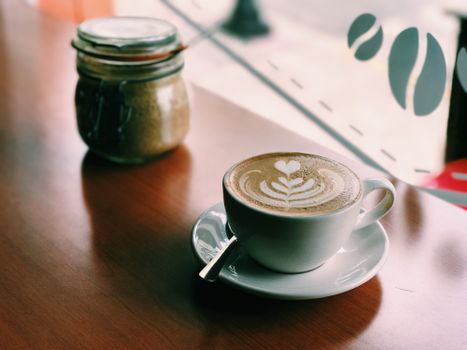 Warm latte with art on wooden table in a cozy cafe, highlighting ambiance and relaxation.