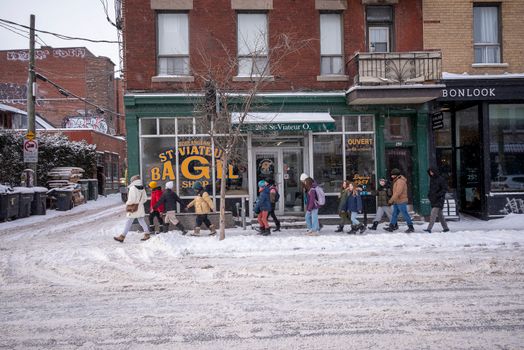 A snowy street scene with pedestrians outside St Viateur Bagel Shop in Montréal.