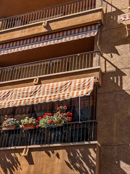 Decorative balconies with striped awnings and flowers in Santiago de la Ribera, Spain.