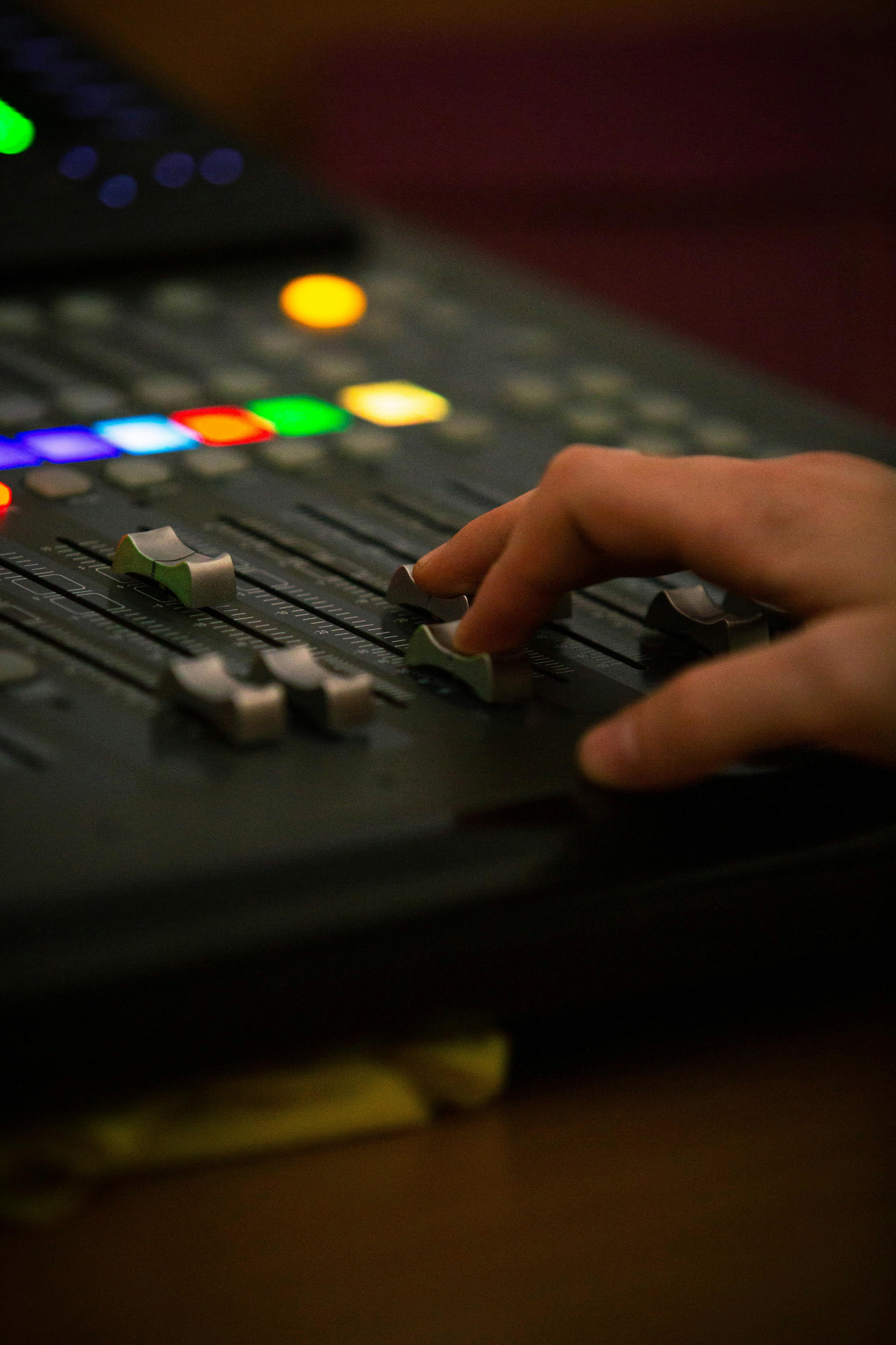 Free A hand adjusting audio mixer controls with colorful buttons and sliders in view. Stock Photo