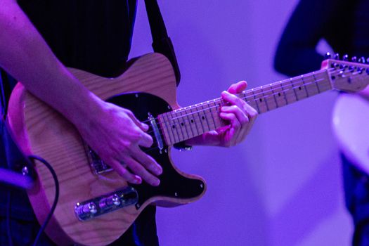 Musician playing an electric guitar on stage with a blue background.