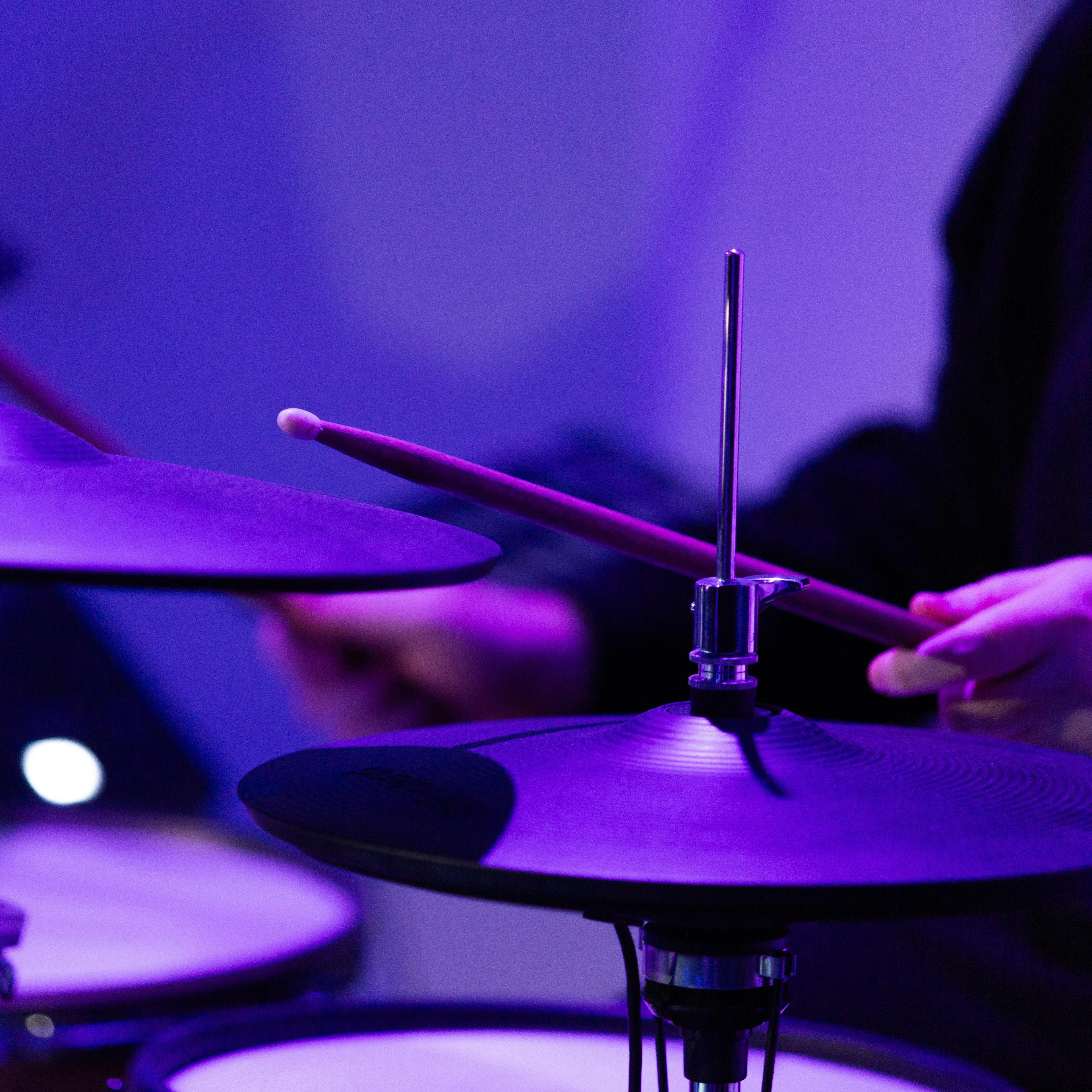 Close-up of a person playing drums with a dramatic purple lighting