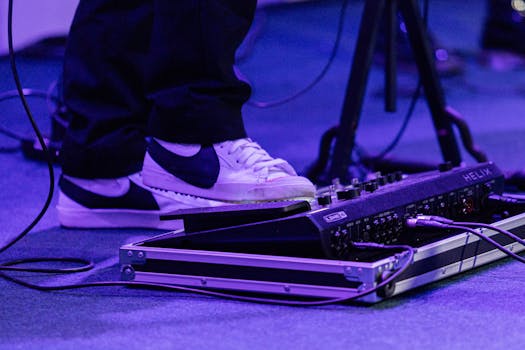 Close-up of a musician's foot on a guitar effects pedal with vibrant stage lighting.