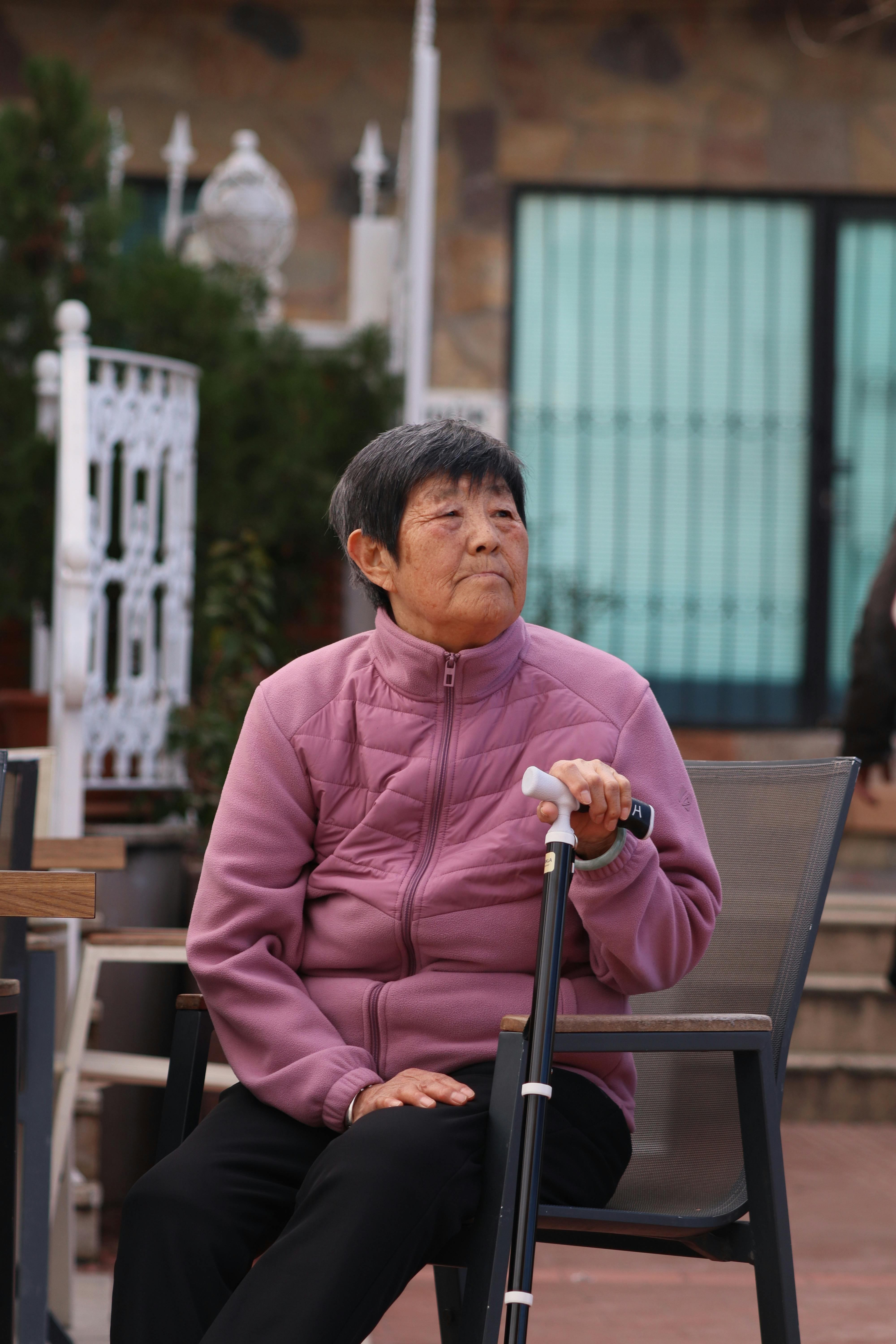 Senior woman in a purple jacket sitting outside with a walking cane in İzmir.