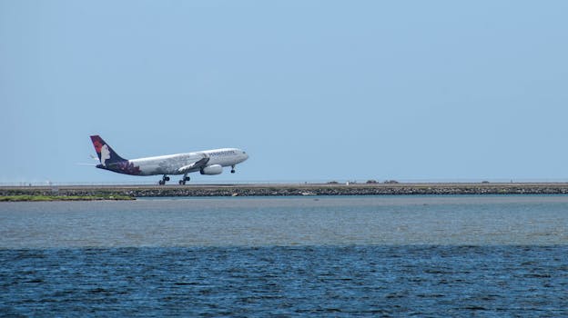 A Hawaiian Airlines plane taking off from a runway near the ocean on a clear day.