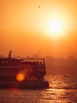 A ferry sails under the warm glow of a sunset on Istanbul's Bosphorus, creating a picturesque view.