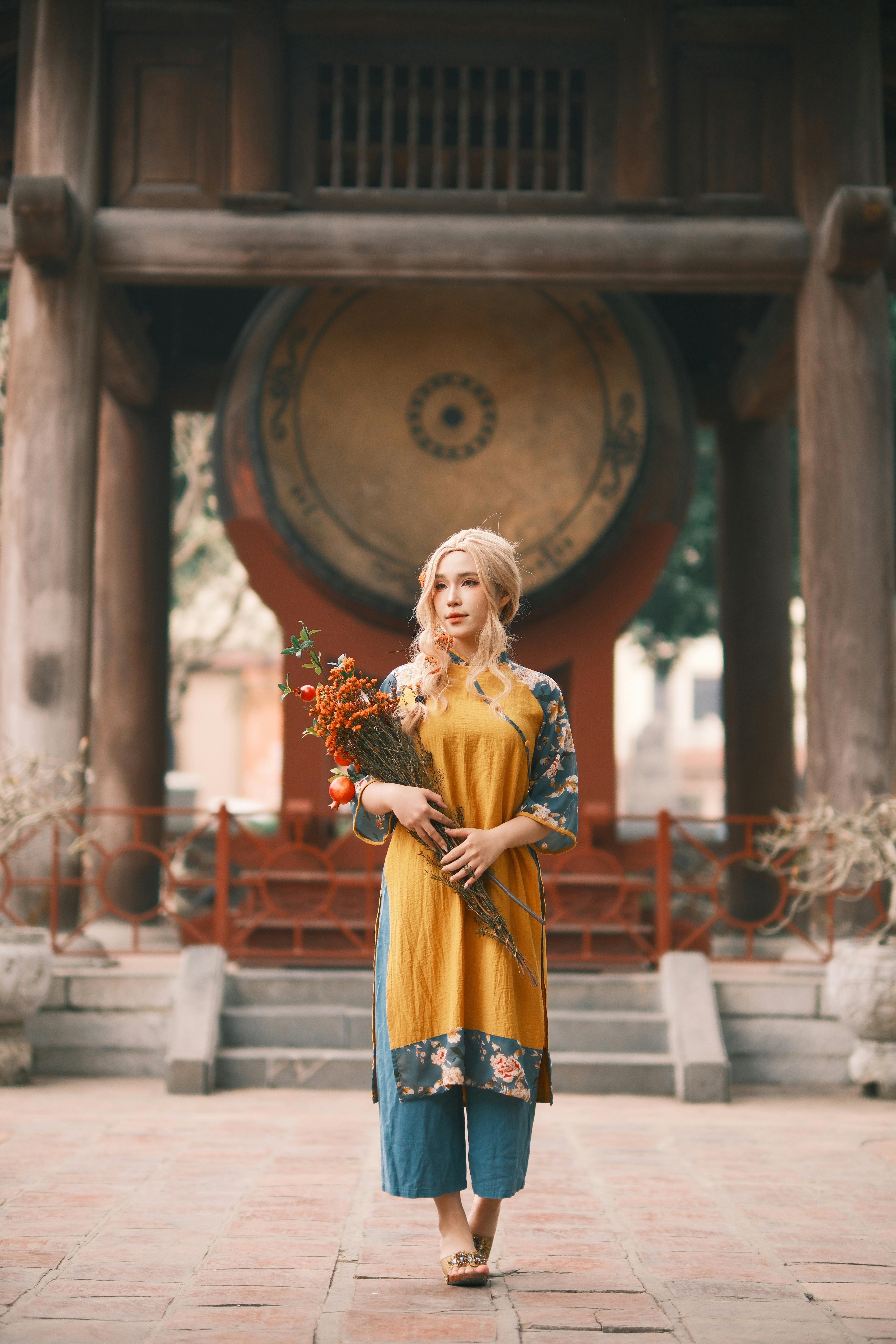 Woman in traditional Vietnamese attire posing in front of a large drum at a temple.