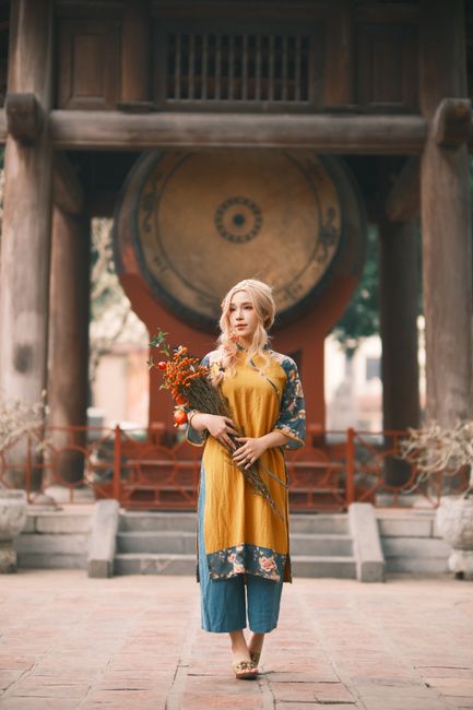 Woman in traditional Vietnamese attire posing in front of a large drum at a temple.