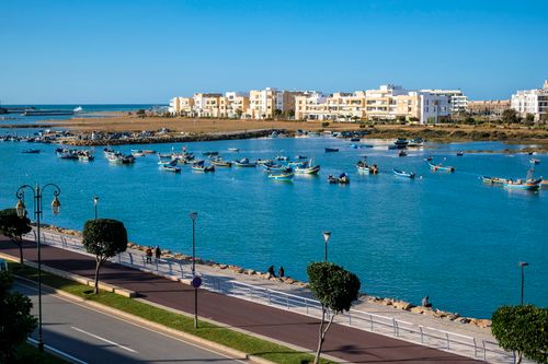 Free A vibrant coastal scene in Rabat, Morocco showing colorful boats and modern architecture. Stock Photo