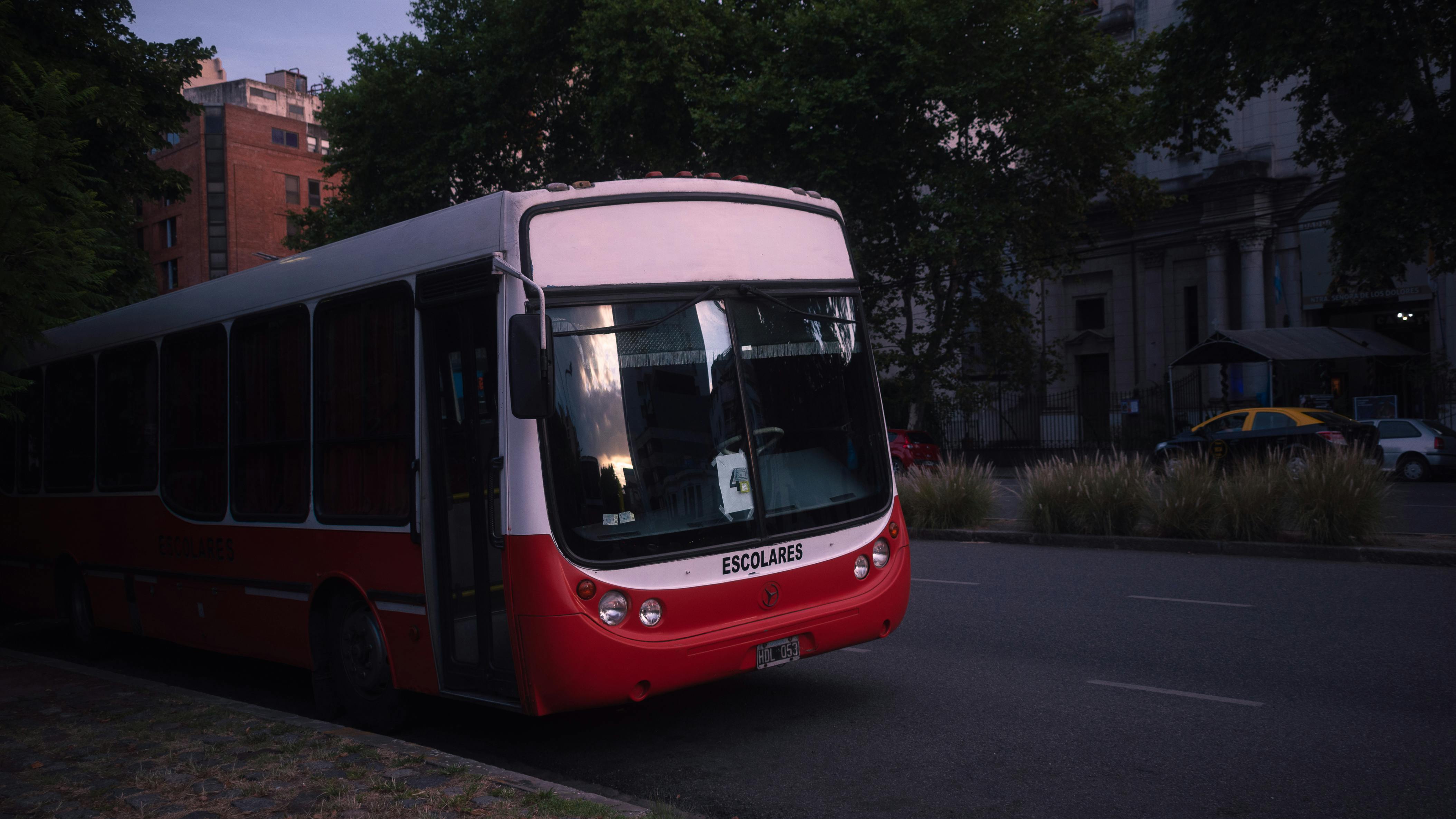 A school bus parked on a quiet street in Buenos Aires during twilight with surrounding urban architecture.