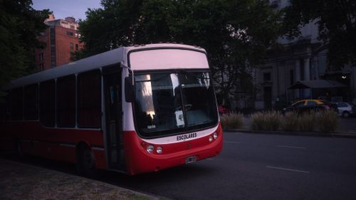 Free A school bus parked on a quiet street in Buenos Aires during twilight with surrounding urban architecture. Stock Photo