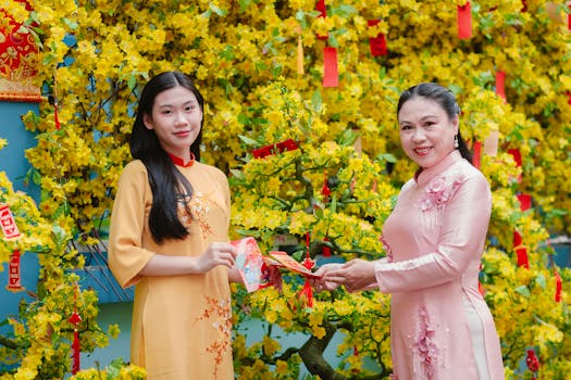 Mother and daughter exchanging red envelopes in front of decorative tree during Lunar New Year celebration.