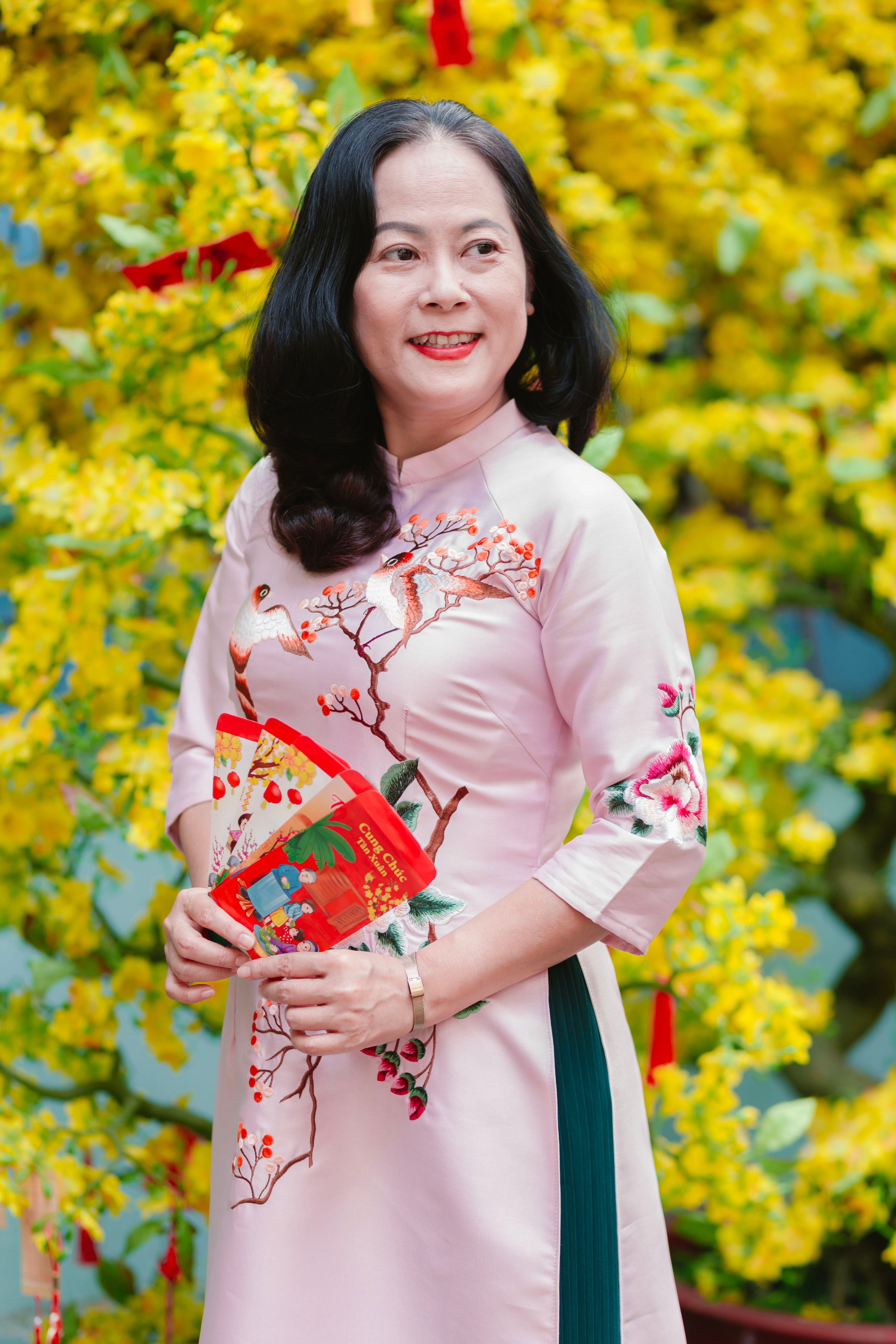 Woman in pink ao dai with Tet decorations holding red envelopes, festive spring atmosphere.