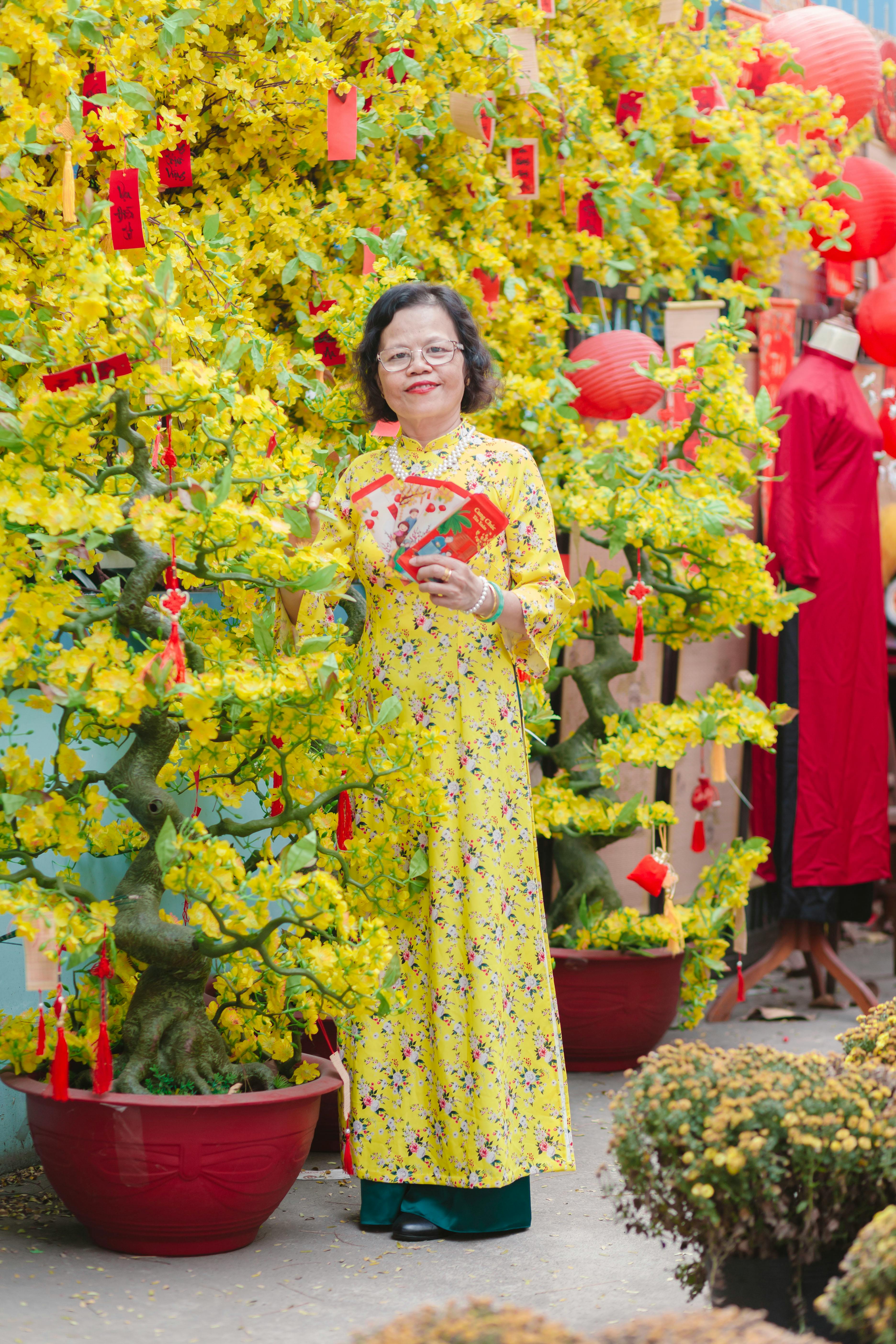 Woman wearing traditional dress celebrates Lunar New Year with yellow blossoms.