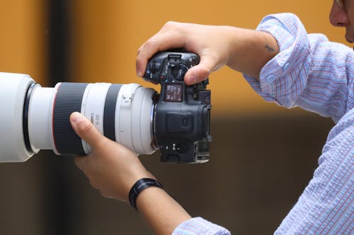 Miễn phí Cận cảnh một nhiếp ảnh gia đang cầm máy ảnh DSLR có ống kính zoom, tập trung vào các chi tiết và độ chính xác. Ảnh lưu trữ