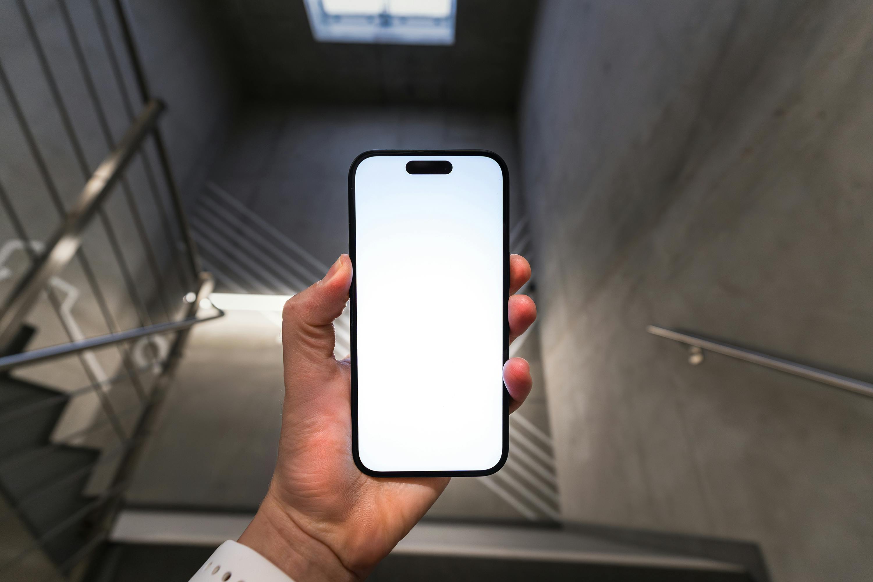 A person holding a smartphone with a blank screen inside a modern stairwell, offering copy space.