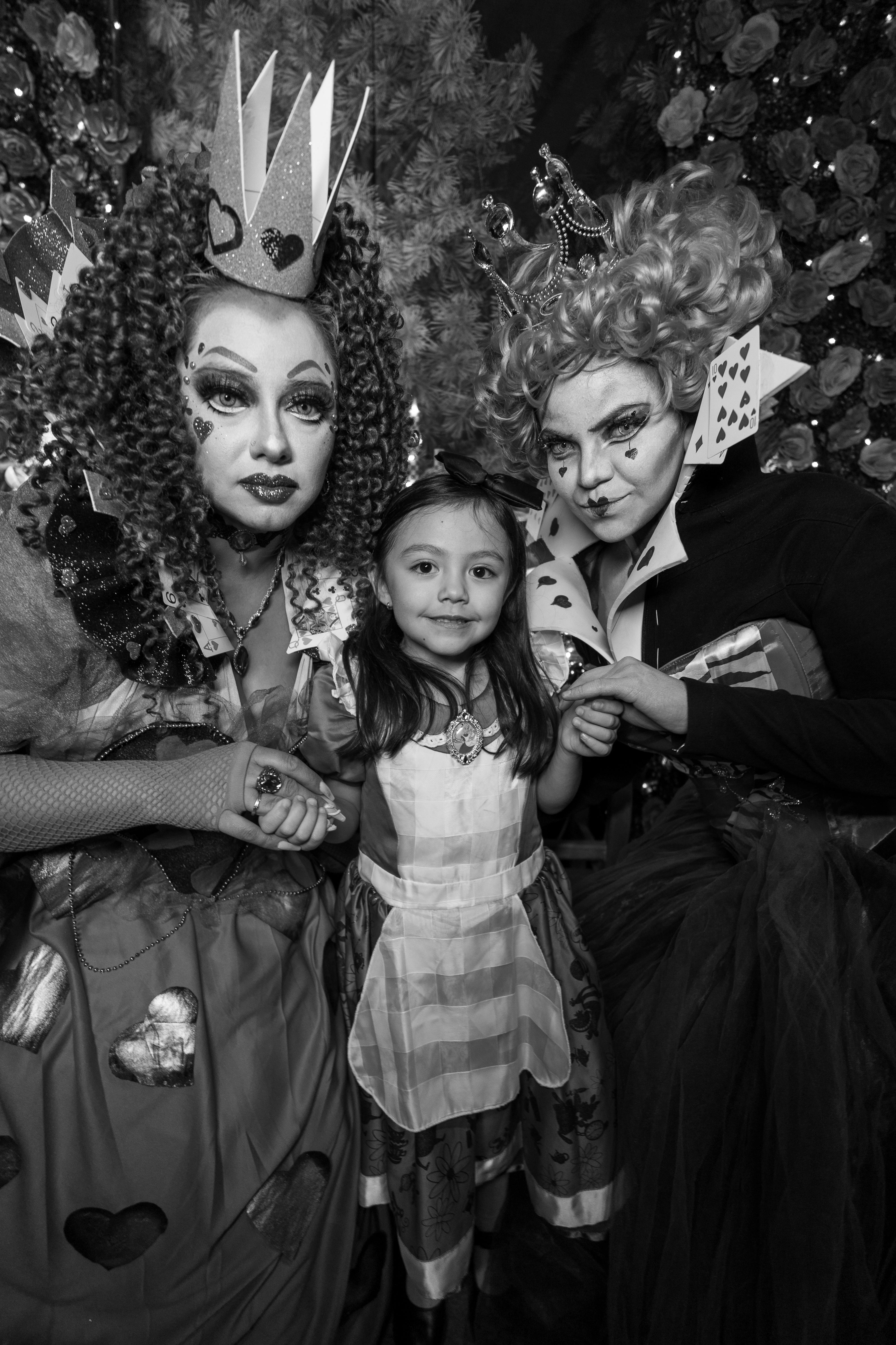 A child with two adults in elaborate Wonderland-themed costumes, vivid artistry.