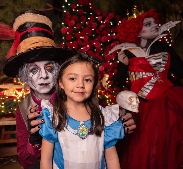Child with Alice in Wonderland character cosplayers at a festive themed party.