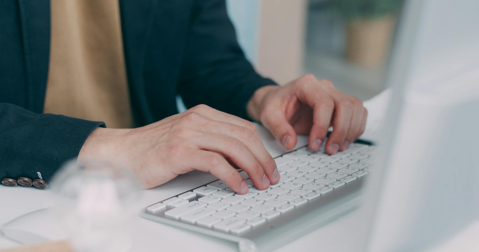 Close-up of hands typing on a white keyboard in an office setting. Ideal for business or technology themes.