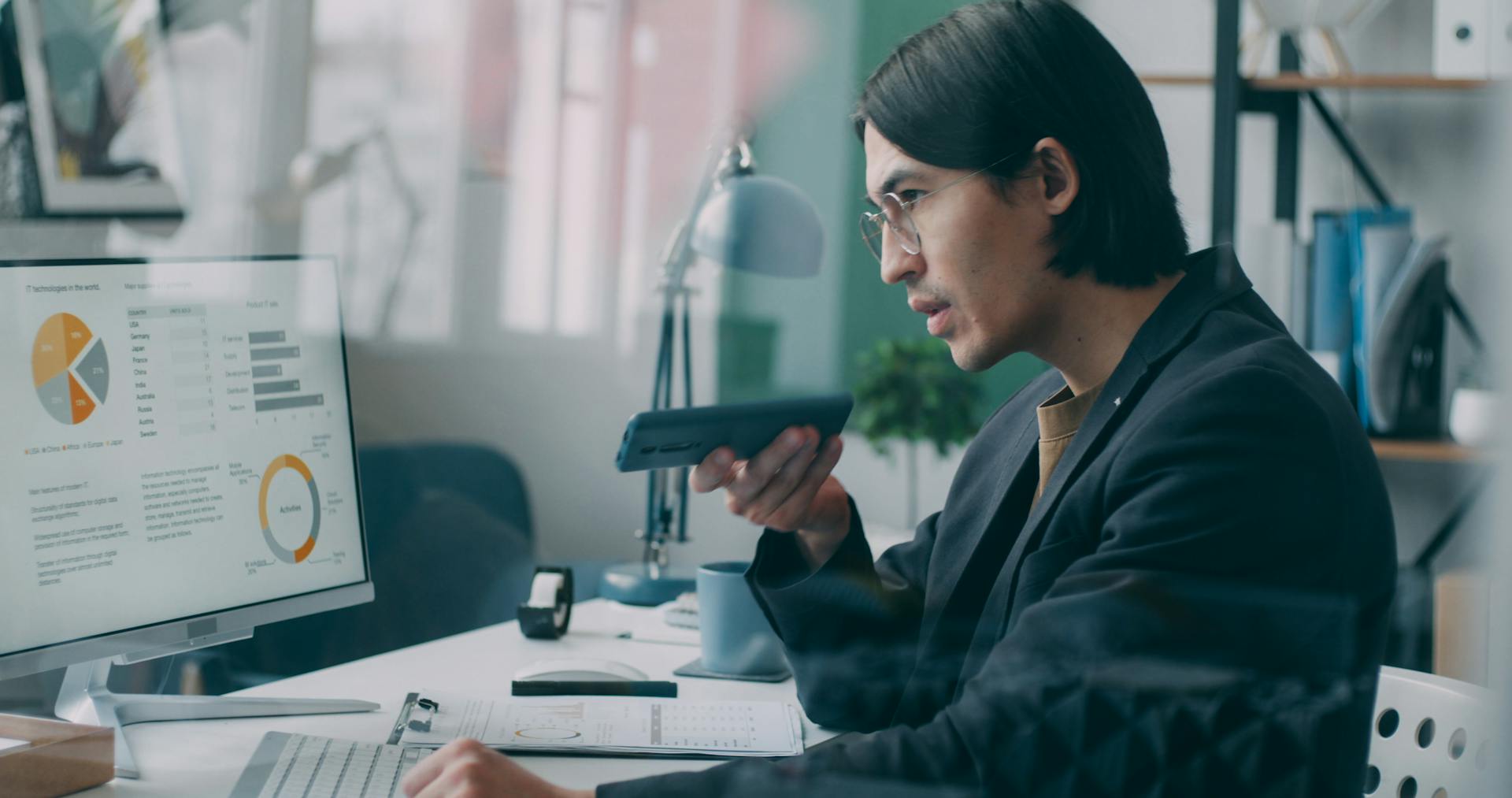 Business professional analyzing data charts on a computer while speaking on phone in an office setting.