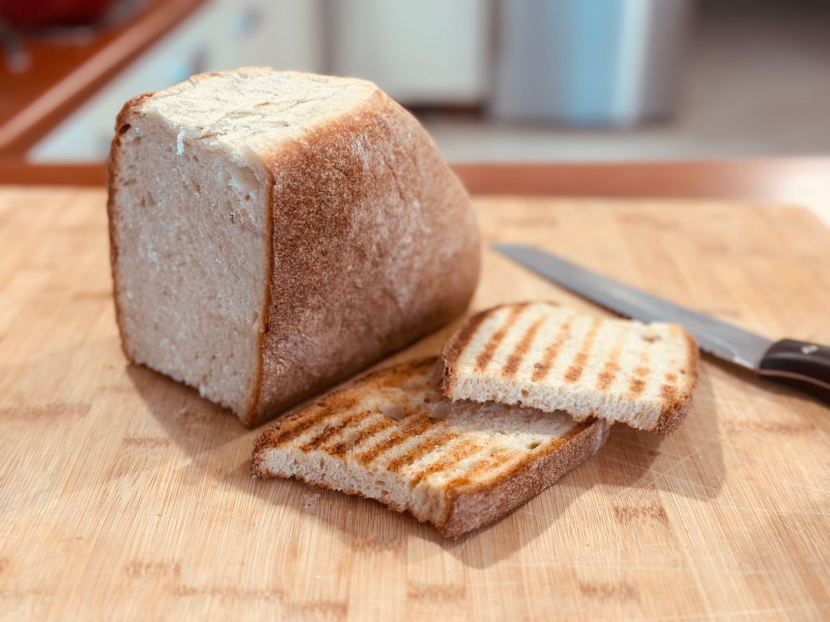 Tall square sandwich loaf with pale crumb beside two grill-marked toast slices and knife