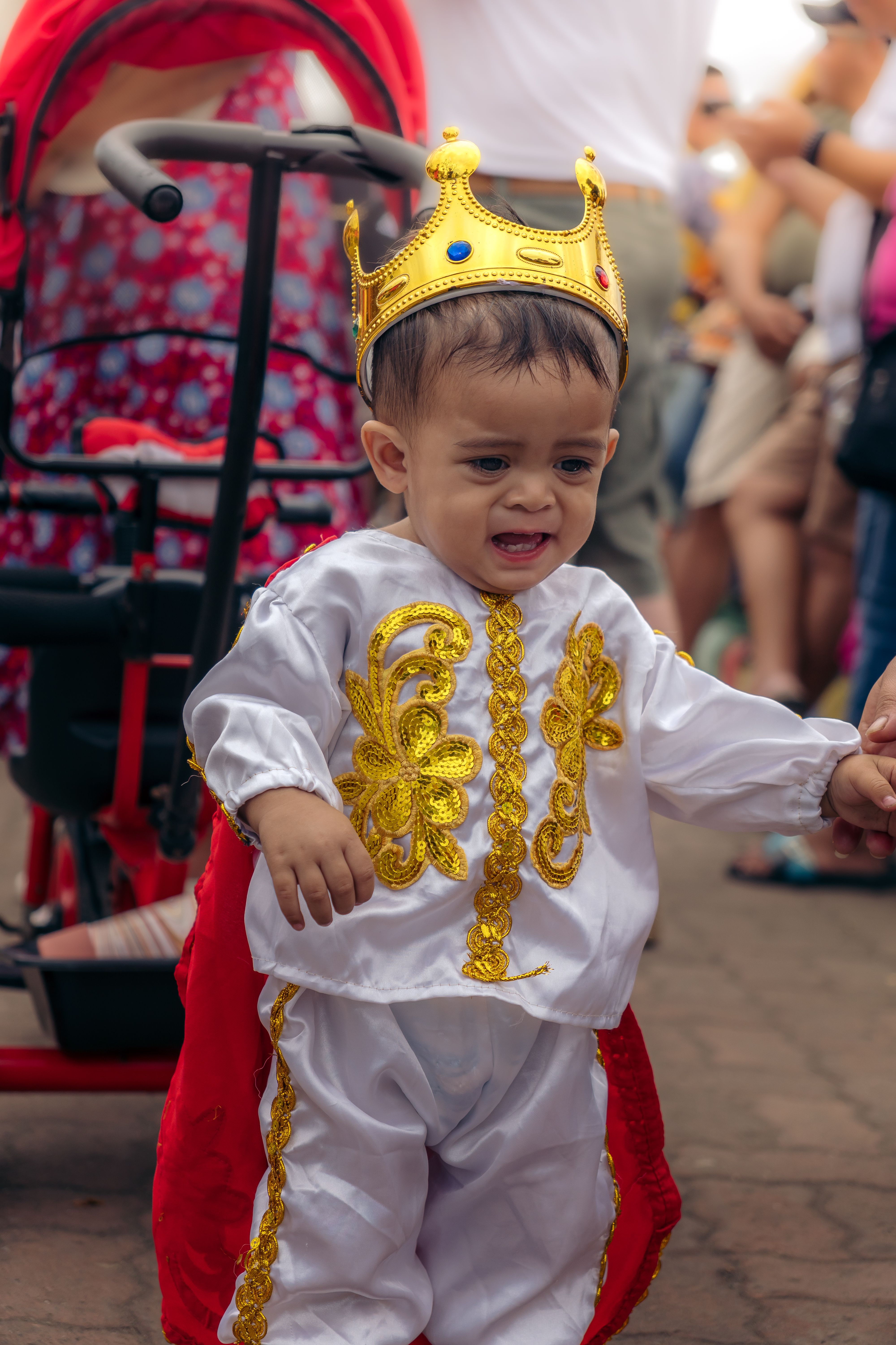 Little child in a royal costume with crown at a lively cultural festival outdoors.