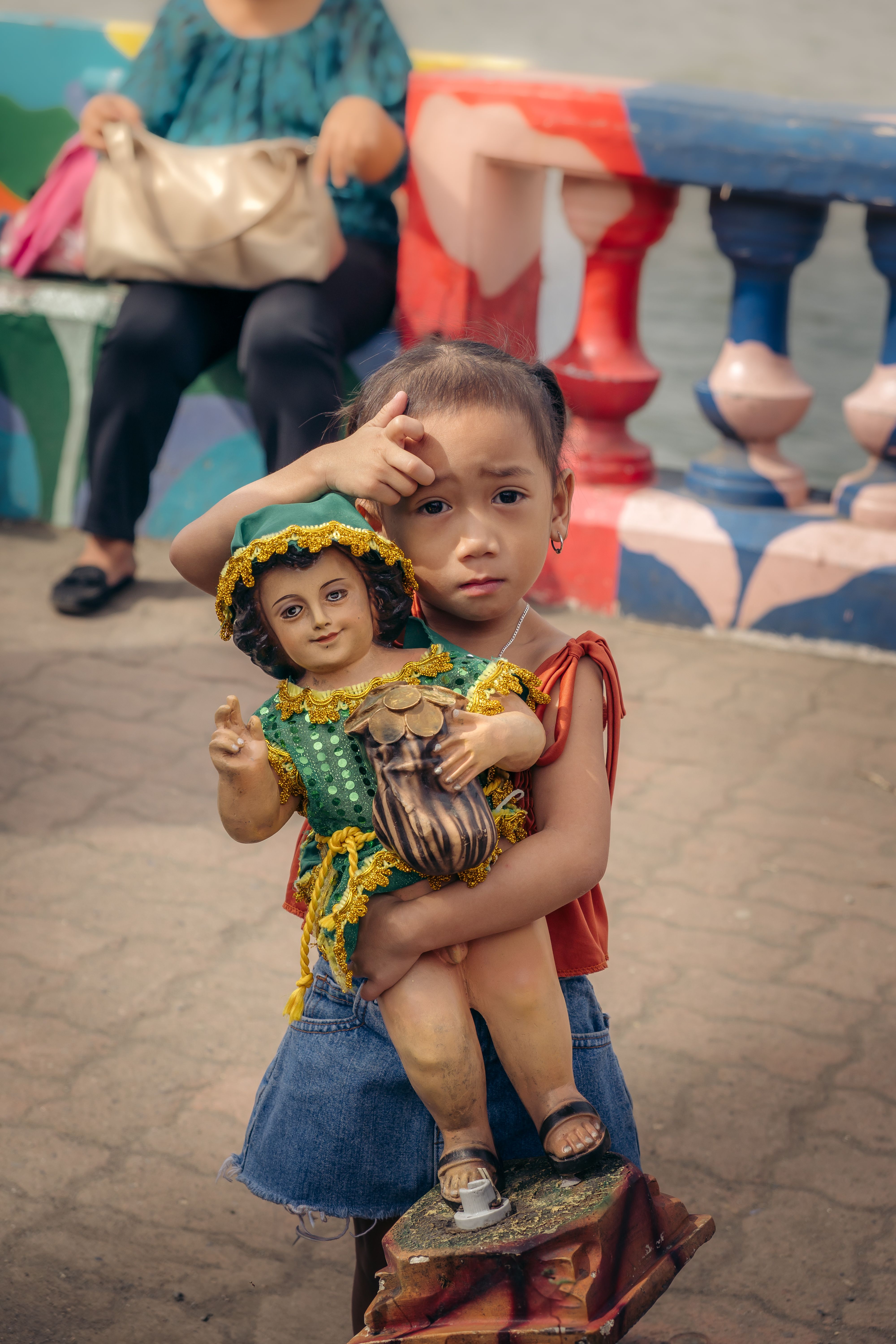 Young child holding a vibrant festive figurine at an outdoor cultural event, bright colors.