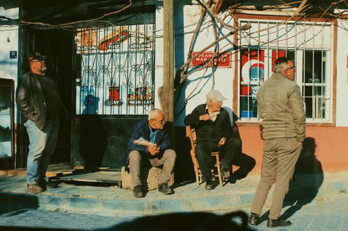 Free Four men enjoy the sun in front of a shop, capturing a moment of daily life. Stock Photo