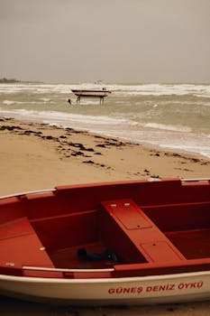 Red boat on a sandy beach with waves and overcast sky, capturing a tranquil coastal scene.