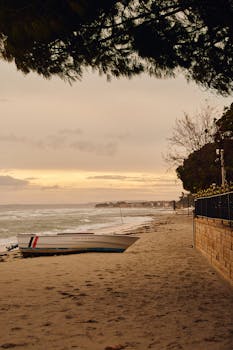 Peaceful beach scene with a boat and gentle waves during sunset.
