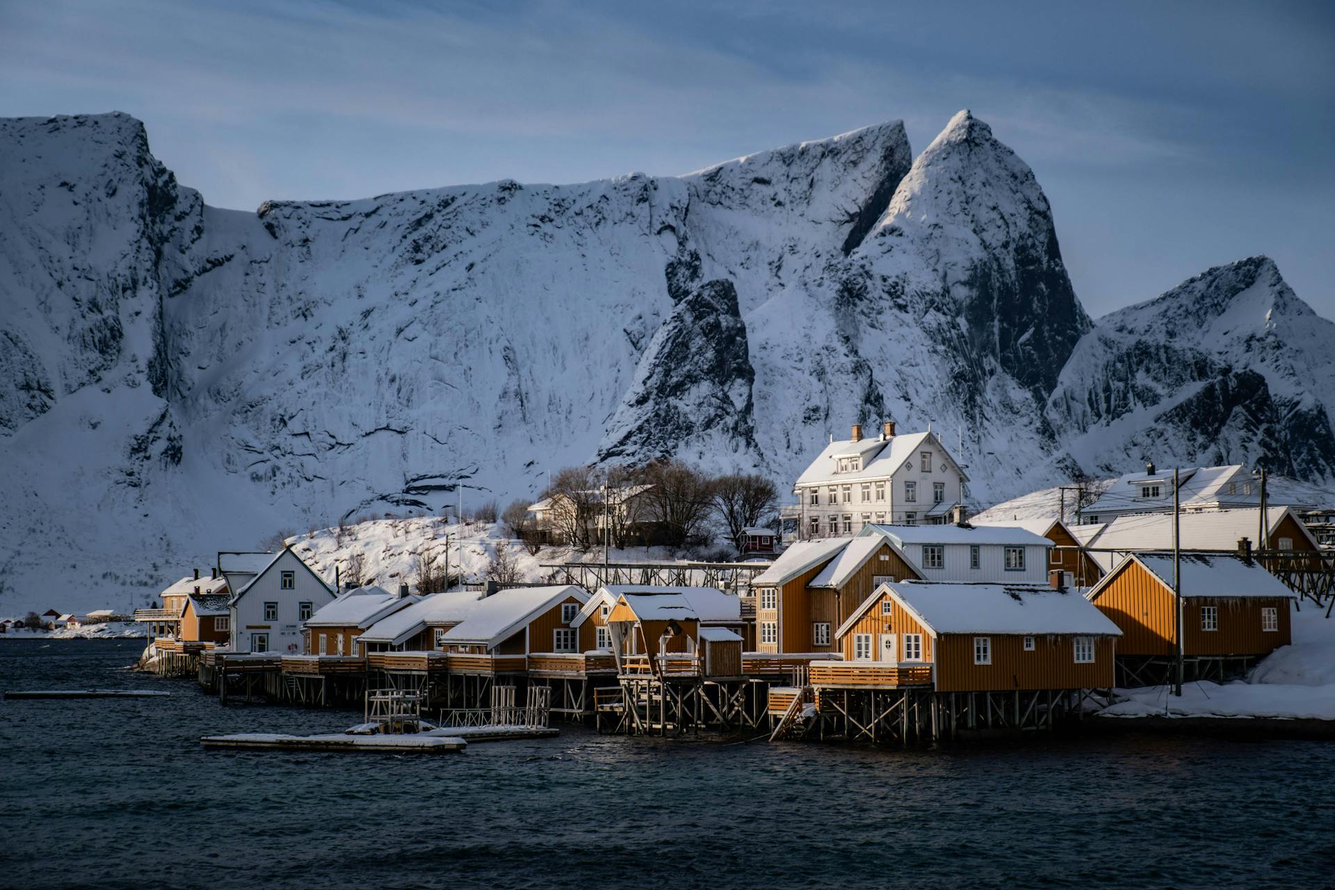 Snow-covered cabins on the Lofoten Islands with dramatic mountain backdrop.