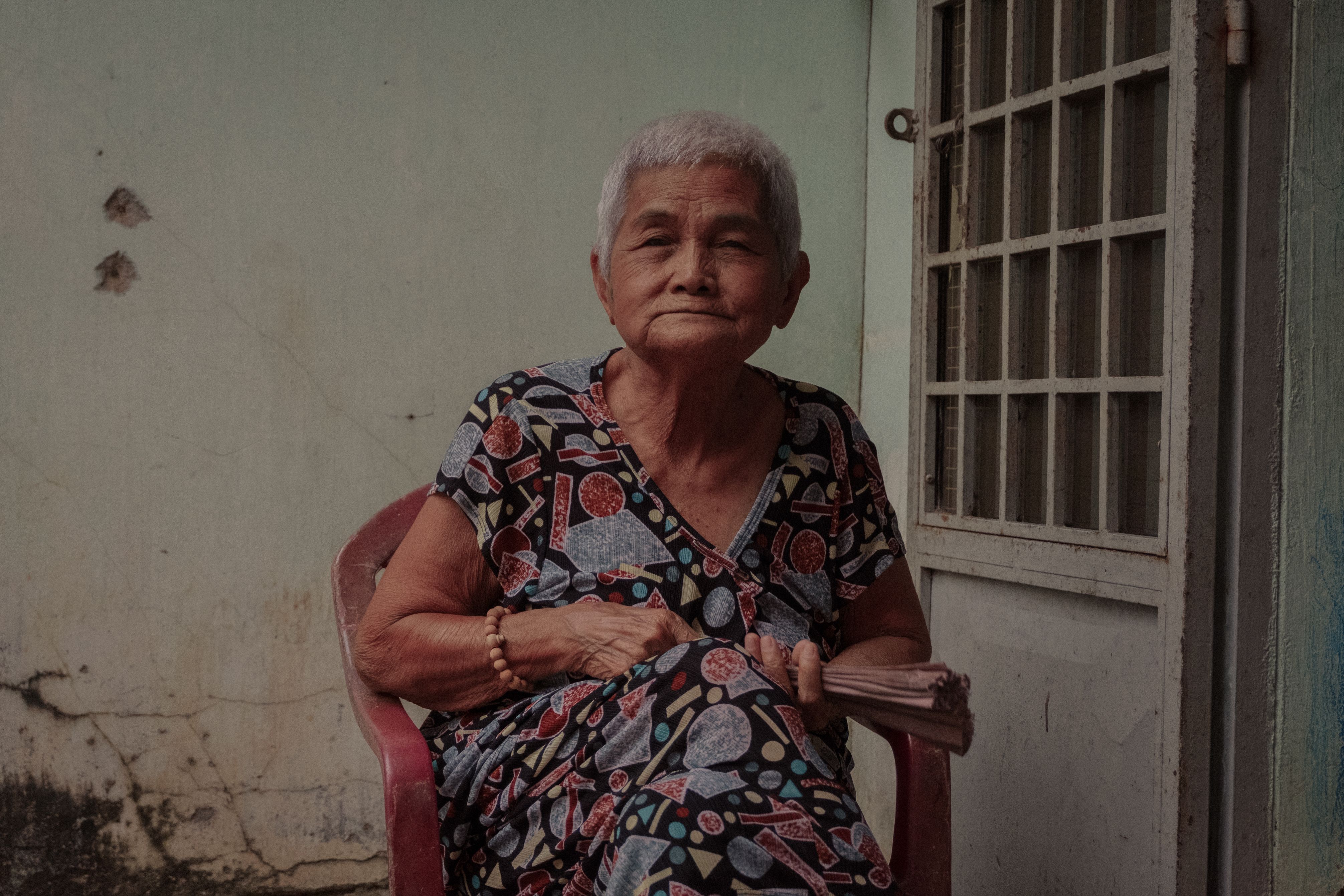 Portrait of an elderly Vietnamese woman sitting outdoors, showcasing traditional attire and serene expression.