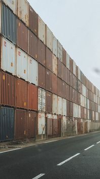 High-rise stack of shipping containers along an industrial road in foggy weather.