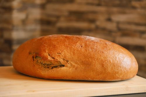 Free Golden-brown rustic loaf of bread on a wooden table, perfect for bakery and food themes. Stock Photo