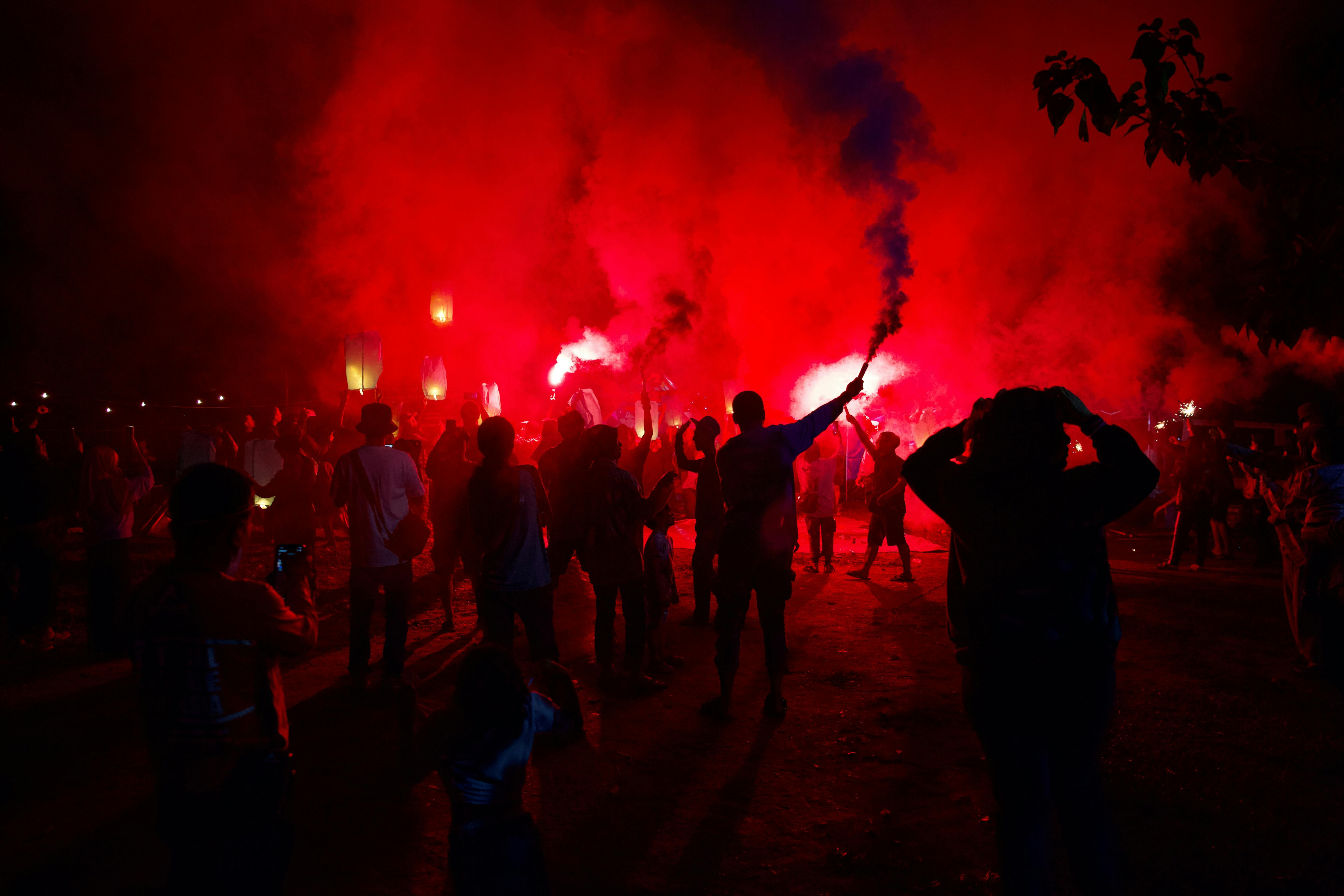 Silhouettes celebrate with red lanterns and smoke in a vibrant night festival in Jakarta.