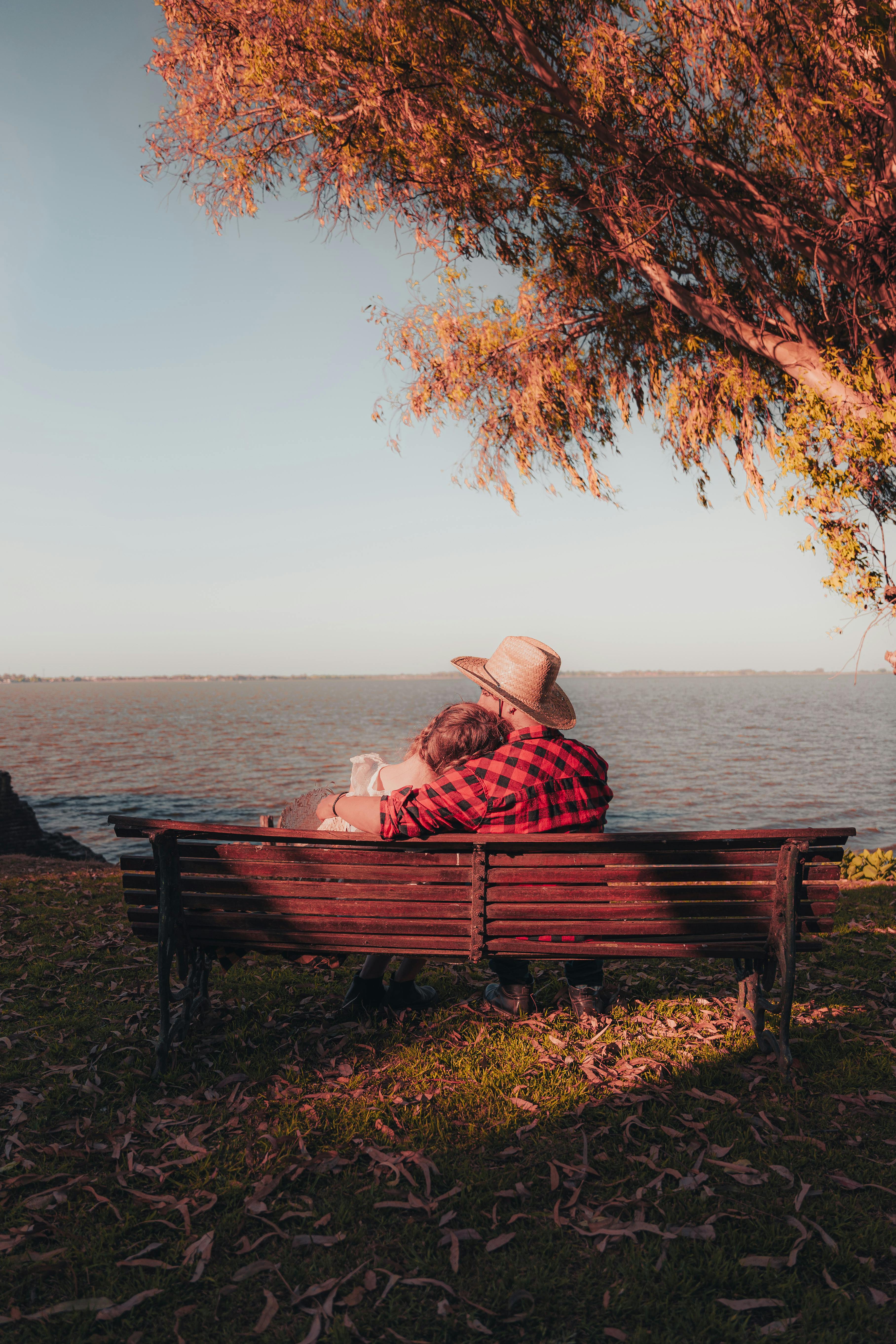 A couple enjoys a serene moment on a park bench beside a lake during autumn.