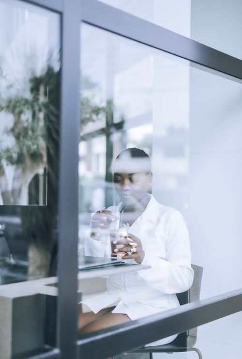 Free Sophisticated woman in white savoring coffee at a stylish café, viewed through glass. Stock Photo