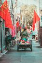 在北京一条狭窄的小巷里，特色是传统建筑、红旗和一名用手推车运送货物的男子