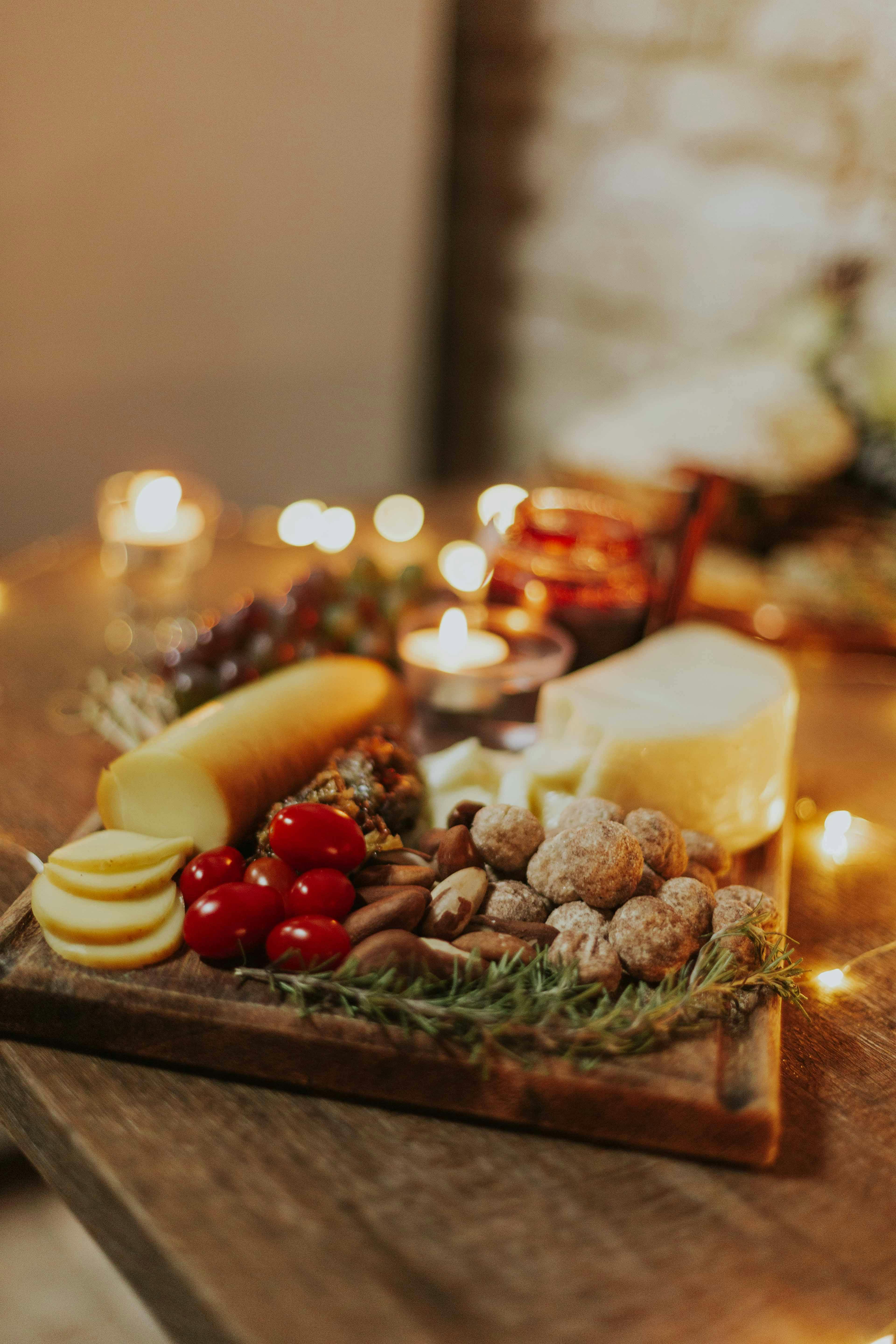 A cozy cheese and charcuterie board with candles, featuring fresh cheeses, nuts, and tomatoes for a festive gathering.