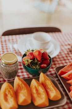 A vibrant assortment of strawberries and melon slices arranged on a checkered table for a summer brunch.