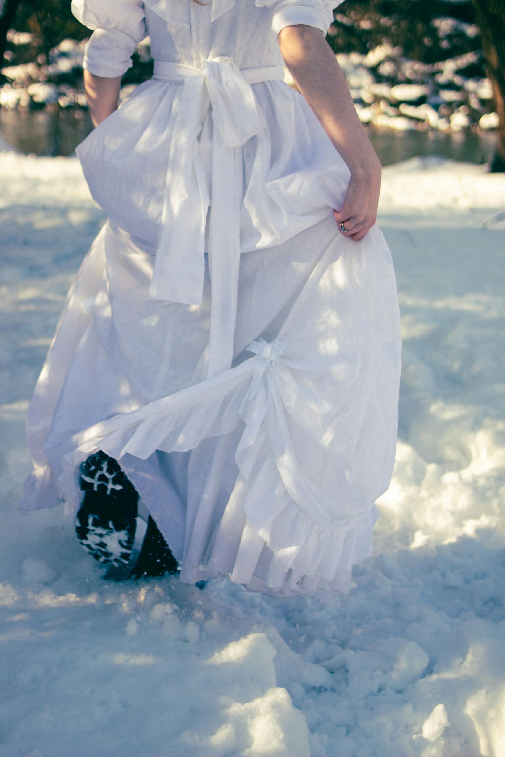 A person in a white dress walks through snow, creating a serene winter scene.