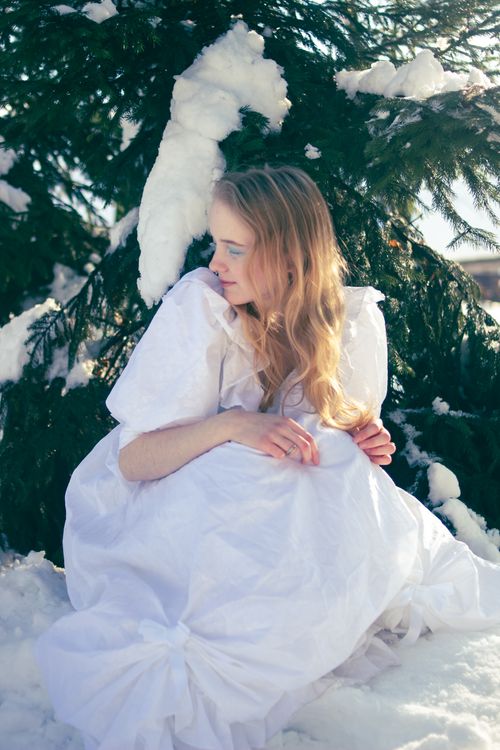 Free A woman in a white dress sits by a snow-covered tree, evoking a serene winter fairy tale. Stock Photo