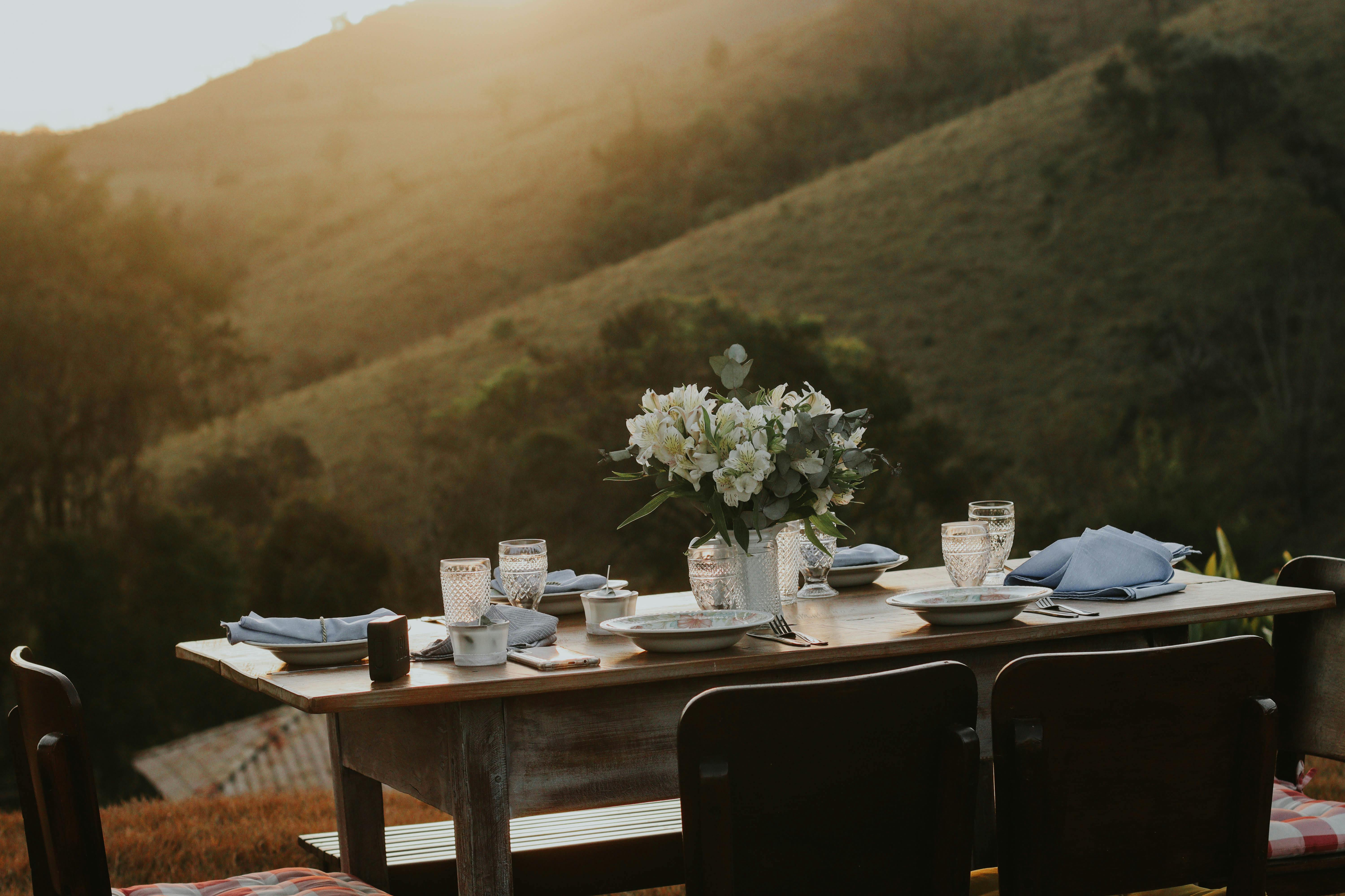 A beautifully arranged dining table outdoors with scenic hills at sunset, creating a serene atmosphere.